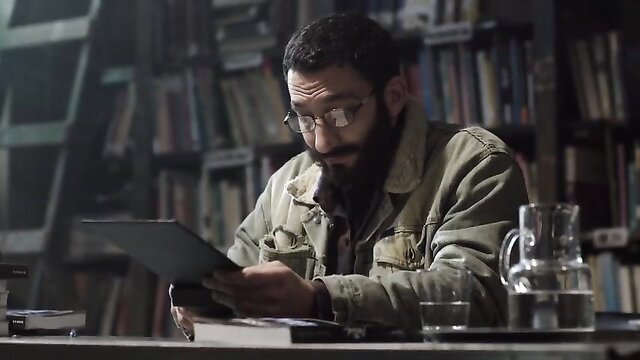 Bearded Latino man in jacket reading tablet in library scene