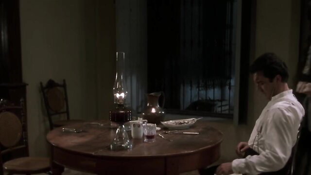 Handsome man in white shirt sits at candlelit table in Original Sin 2001