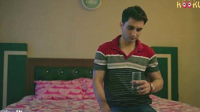 Handsome Desi guy in polo shirt sits pensively on bed holding glass