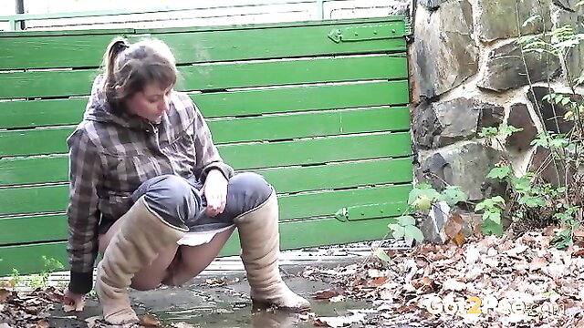 Cute brunette country girl in plaid shirt pees behind fence in boots