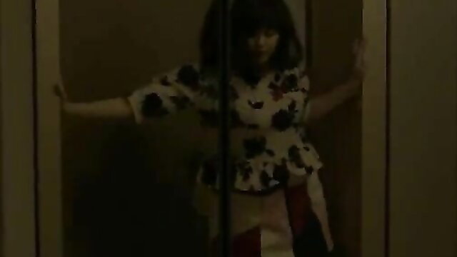 Young Asian woman in floral blouse and skirt poses seductively in doorway