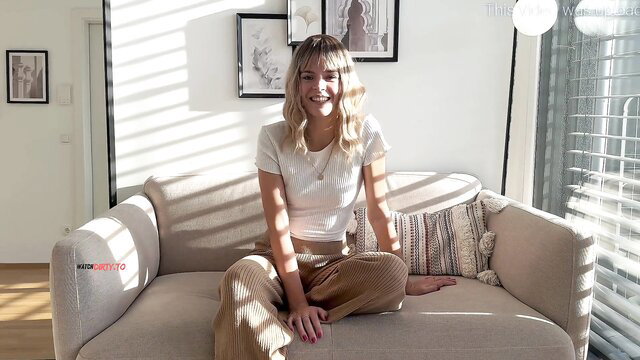 Arabella-Spitz blonde smiling on couch in white top and pants