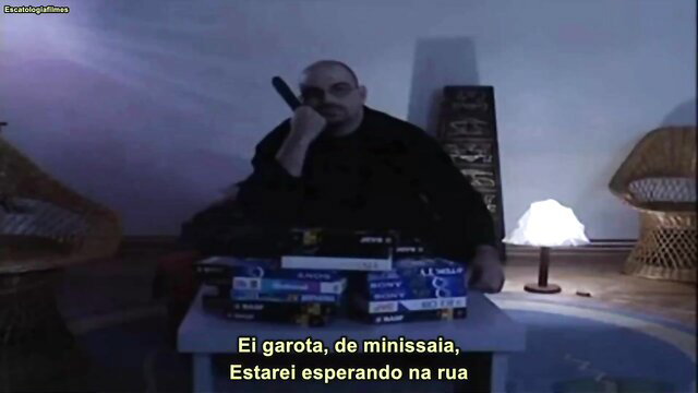 Bald Latino man in dark shirt with porn DVDs, waiting girl on street