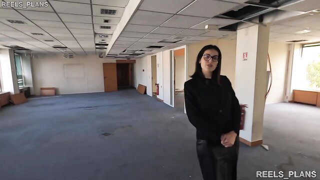 French brunette in glasses poses in empty office, leather pants