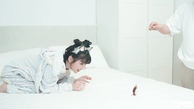 Japanese catgirl in fluffy robe on bed reaching for tiny cock toy