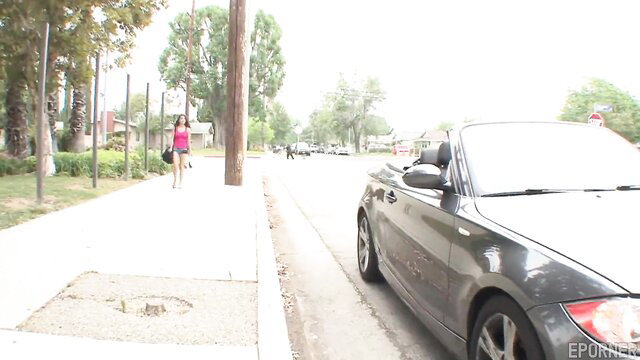 Brunette in pink walking by BMW on street, sunny day