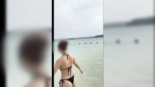 Fit Asian woman in black thong bikini walking into shallow beach water