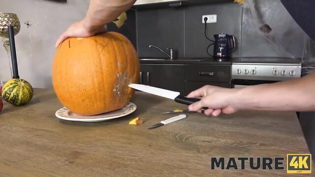 Mature brunette carving pumpkin with knife in kitchen, MATURE4K