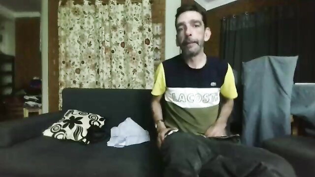 Amateur Latino man in Lacoste shirt on couch, explicit adult video thumbnail