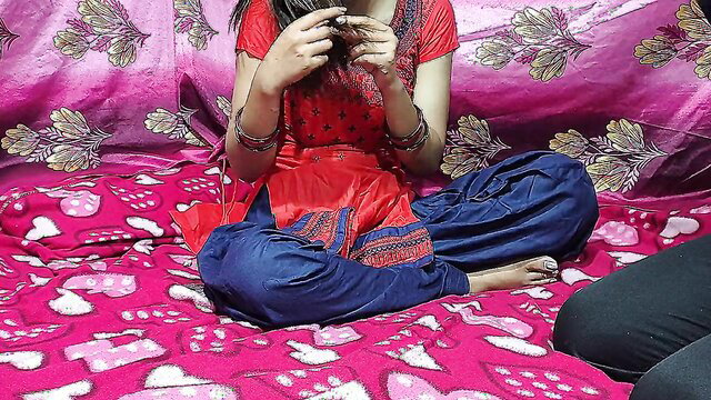 Indian teen in red salwar kameez sits cross-legged on bed, teasing