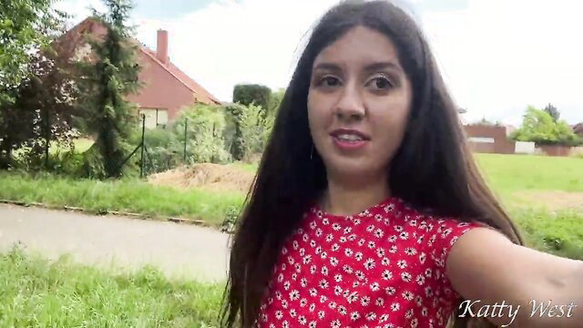Katty West smiles in red polka dot top, long dark hair, park walk