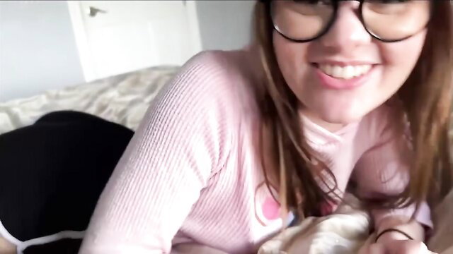 Alex Adams smiling in pink sweater and glasses on bed, teasing thumbnail