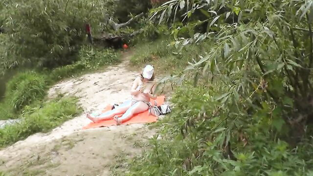 Topless MILF sunbathing nude on wild river bank, peeping passerby