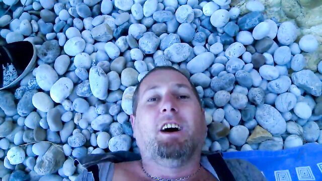 Terry Reid lying on pebbles beach, shaved head grinning up at viewer