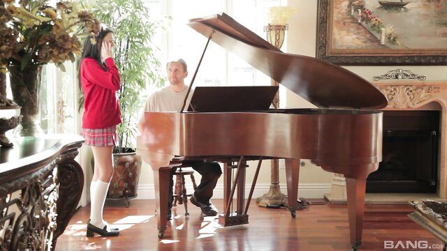Megan Piper in schoolgirl skirt stands by piano with man in Dirty Little Stories