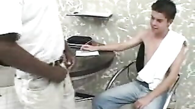 Black man stands over seated white twink sucking huge cock