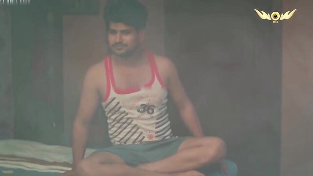 Horny Indian guy in tank top and shorts sits on bed, muscular build