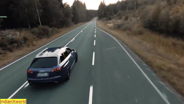 Blue Audi A6 Avant wagon driving on curvy rural road at sunset