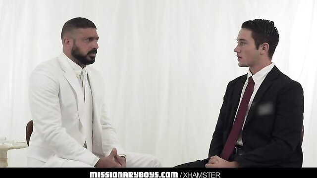 Bearded man in white suit faces young suited guy in Missionary Boys gay priest scene