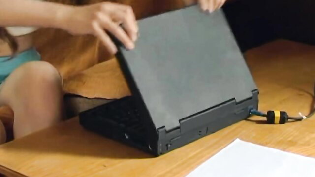 Slim Asian teen in shorts opening laptop on couch