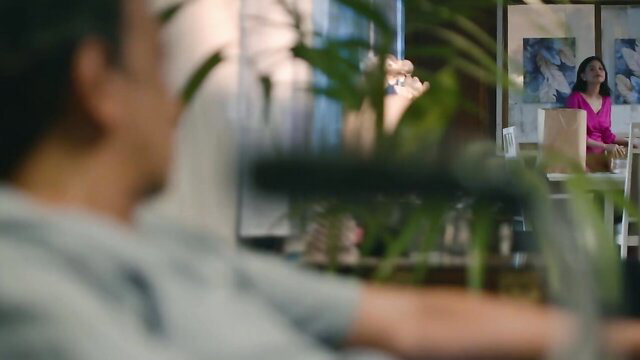 Asian office woman in pink blouse at desk, blurred foreground view