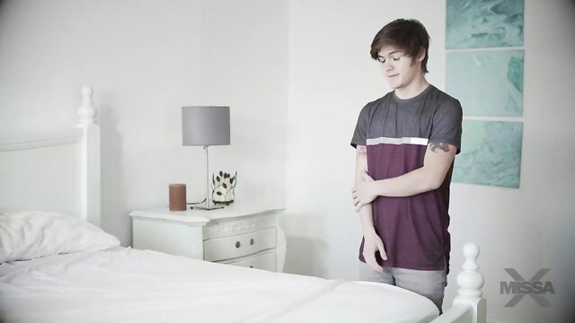 Young man in bedroom stands arms crossed grey shirt shorts Missax