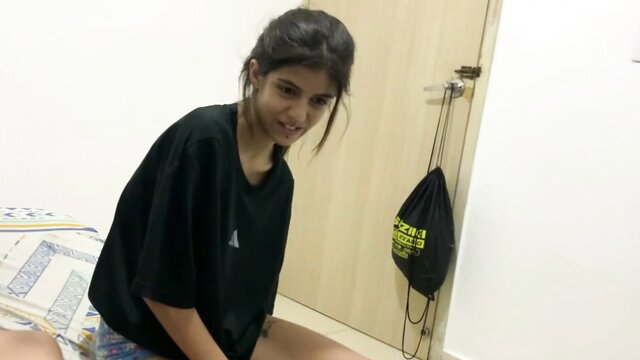 Horny Indian step sister in oversized tee and shorts smiles teasingly in bedroom