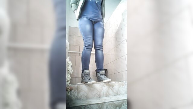 Blonde girl in tight blue jeans and sneakers stands in bathroom