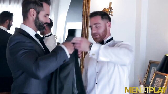Handsome suited men helping each other dress in tuxedos at formal event