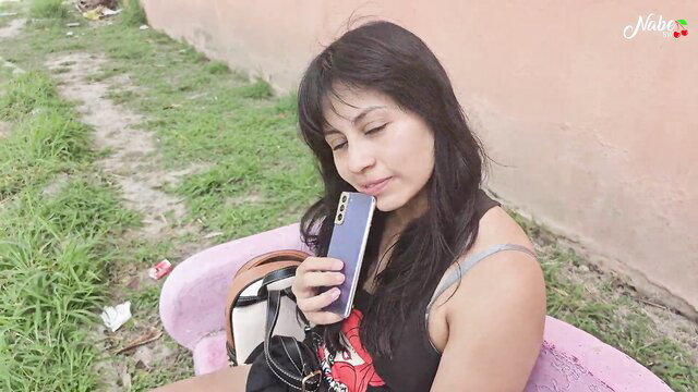 Latina babe in tank top sits outdoors holding phone, amateur tease