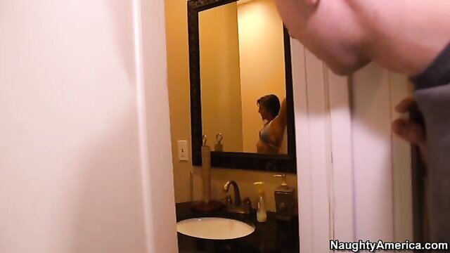 Mischa Brooks in bra admiring mirror reflection in bathroom