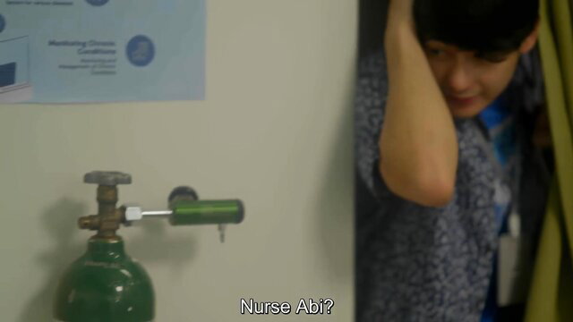 Nurse Abi peeking from curtain by oxygen tank in hospital room