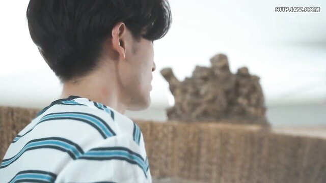 Handsome Asian man in striped shirt, profile view by beach rocks