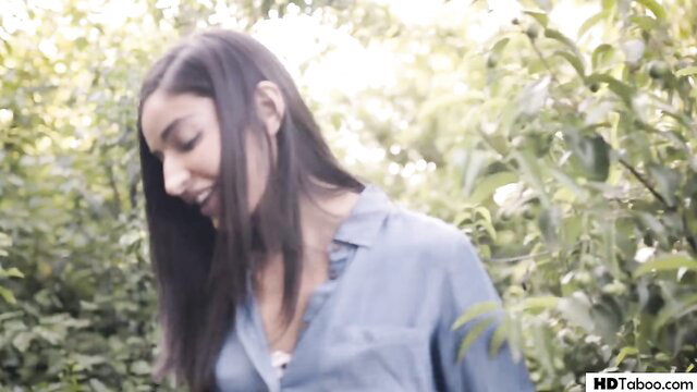 Brunette beauty in blue shirt smiles in lush garden, Pure Taboo lesbian tease