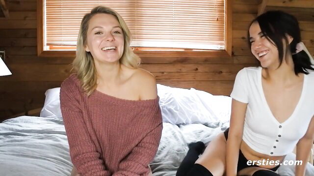 Two smiling amateur girls on bed, one off-shoulder sweater, other short dress thigh-highs