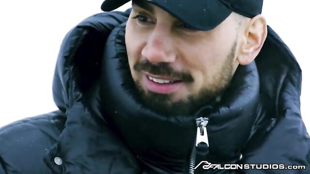 Hot muscular bodybuilder in black puffer jacket and cap smirks outdoors