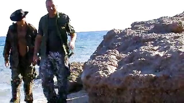 Lorena Sanchez with muscular men on rocky beach in army gear
