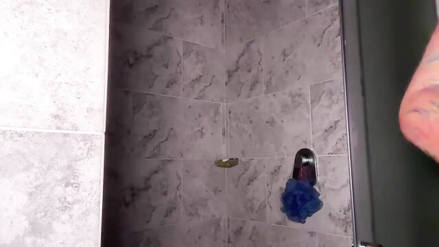 Tattooed woman in shower with loofah, nude ass view