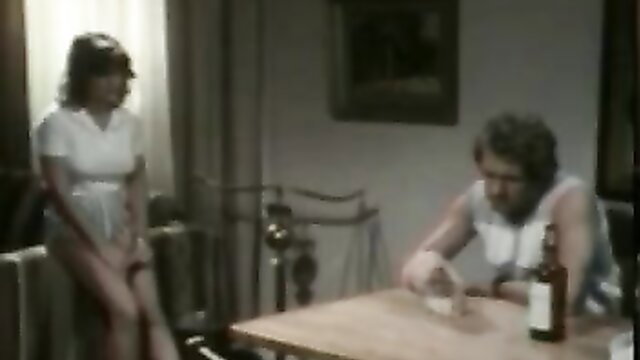 Vintage 1984 porn thumbnail: brunette in white dress stands over man drinking at table
