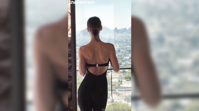 Rachel Cook back view in tight black backless dress on balcony