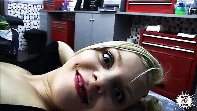 Blonde tattoo girl smiling playfully on chair in shop, red lips