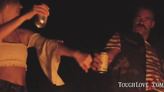 Kenna James exchanges drinks with mustached man by campfire at night
