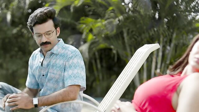 Indian couple lounging poolside, busty woman in red top smiles at man in Hawaiian shirt