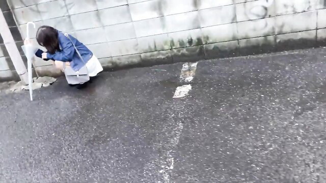Japanese schoolgirl in skirt squatting on wet street, upskirt tease