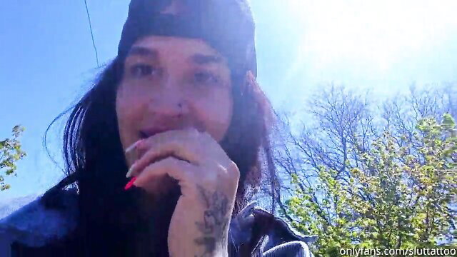 Tattooed brunette in cap poses seductively outdoors, OnlyFans promo