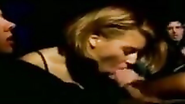 Blonde woman in black top passionately kissing man in dim light