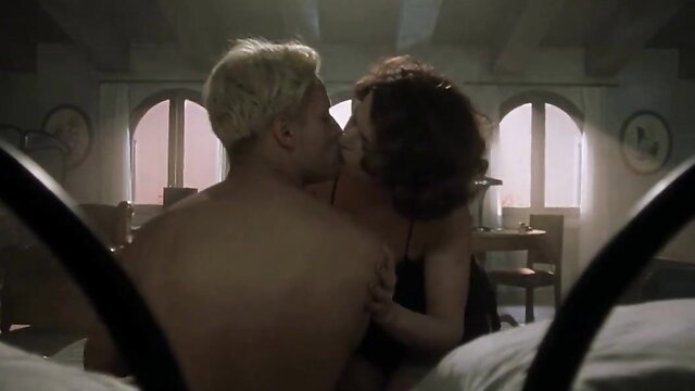 Blonde guy kissing redhead woman passionately on bed in steamy scene