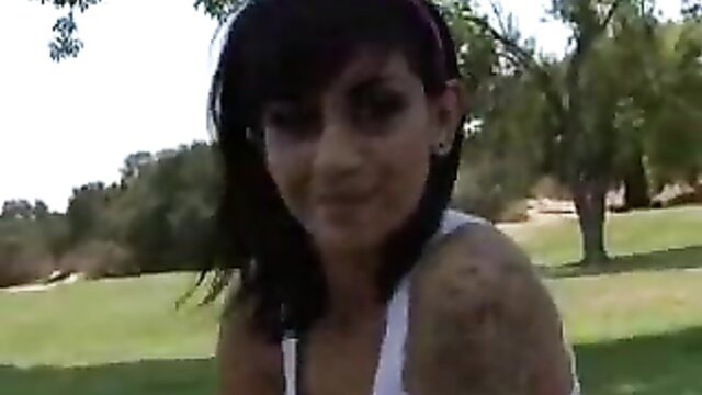 Kayden Faye smiles outdoors in tight white tank showing tattoos and cameltoe