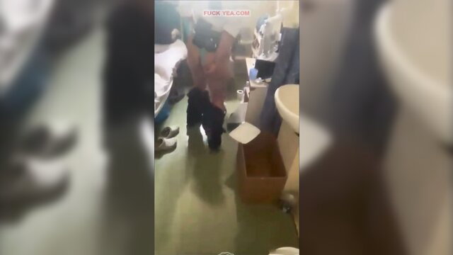 Prison guard in uniform bends over toilet in cell with inmates