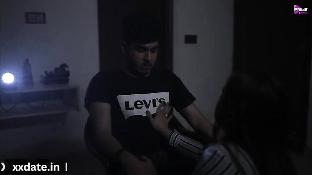 Indian guy in Levi's shirt holds woman's hand intimately in dim room